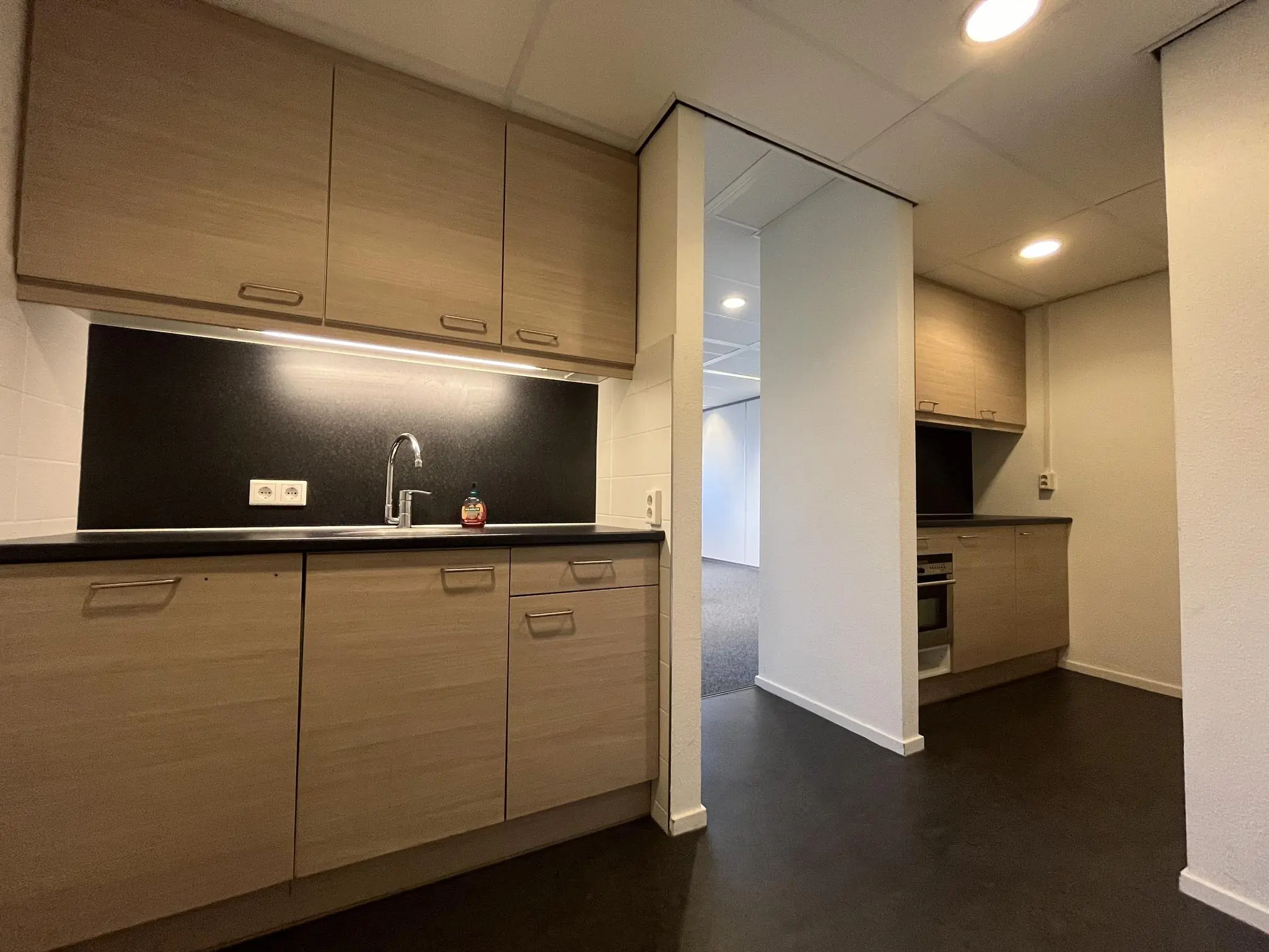 Moderne keuken met houtkleurige kasten, zwarte achterwand en ingebouwde oven aan de Baarnsche Dijk.